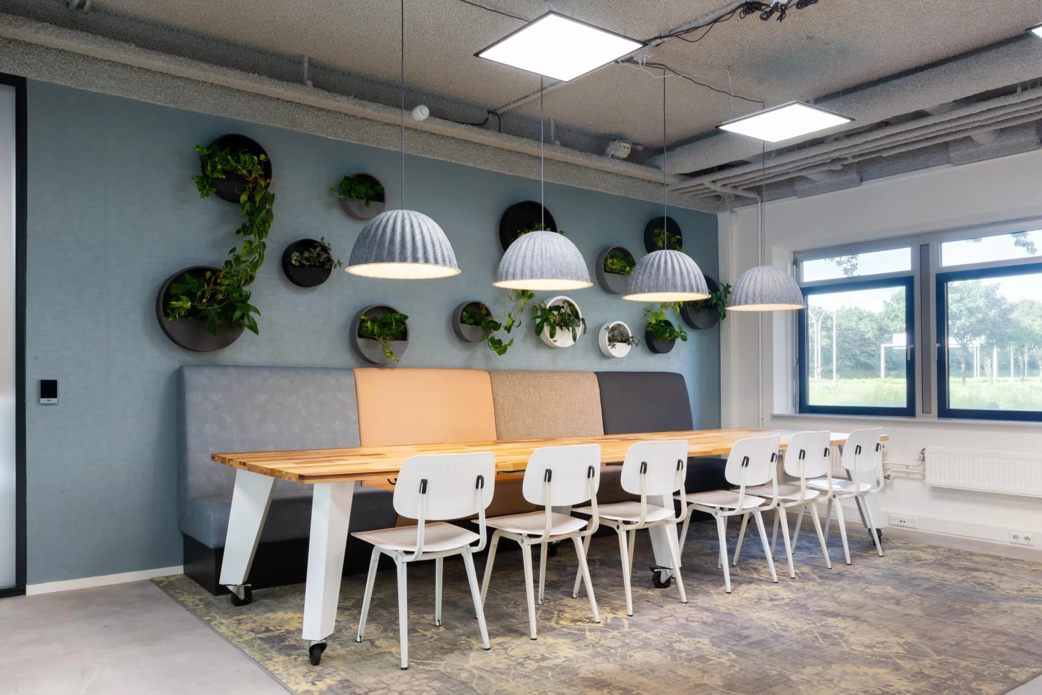 Overlegruimte met lange tafel, banken en een groene wand, ontworpen door Beijer Advies